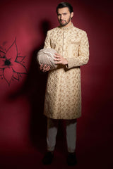 Arsalan Iqbal gold silk sherwani featuring intricate floral ivy embroidery, an embellished mandarin collar, and matching cuffs, paired with ivory trousers and a coordinated silk turban.
