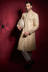 Arsalan Iqbal champagne gold silk sherwani with floral ivy embroidery, featuring a model in a cross-legged pose holding a matching silk turban.