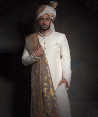 Front portrait of Arsalan Iqbal luxury ivory sherwani with diamond-textured fabric, featuring a gold-embroidered mandarin collar, styled with a gold-bordered grey silk shawl and a matching gold-striped turban.