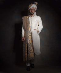 Full-length portrait of Arsalan Iqbal luxury ivory sherwani with diamond-textured fabric, featuring an embroidered mandarin collar, a gold floral silk shawl, matching ivory trousers, and black formal loafers.