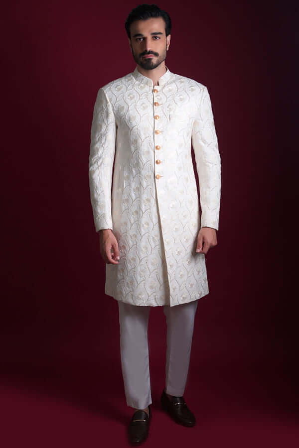 Full-length view of Arsalan Iqbal luxury ivory sherwani featuring an all-over pearl-white floral vine pattern on silk, with a mandarin collar and gold-toned buttons, paired with white trousers.