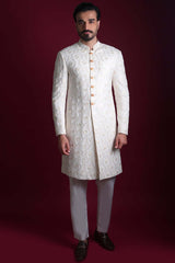 Full-length view of Arsalan Iqbal luxury ivory sherwani featuring an all-over pearl-white floral vine pattern on silk, with a mandarin collar and gold-toned buttons, paired with white trousers.
