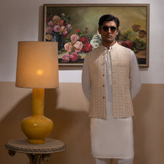 Arsalan Iqbal Light Gold Embroidered Waistcoat with IronEZ Kurta & Pyjama Set man wearing a light gold heavily embroidered sleeveless waistcoat with gold button closure over a crisp white full-sleeve kurta, paired with matching white straight-cut pyjama, accessorized with sunglasses, styled in a warm classic indoor setting