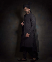 Side profile view of Arsalan Iqbal midnight black luxury sherwani featuring spaced-out tonal motifs, styled with a high-pleated black turban, matching trousers, and traditional khussa shoes.