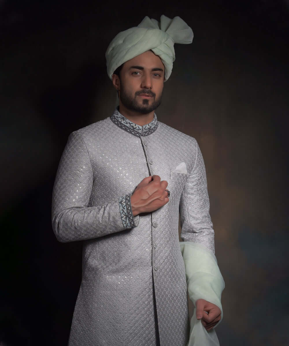 Mid-length portrait of Arsalan Iqbal mint green luxury sherwani featuring silver geometric embroidery, a charcoal grey embroidered mandarin collar and cuffs, styled with a matching mint turban.