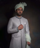 Mid-length portrait of Arsalan Iqbal mint green luxury sherwani featuring silver geometric embroidery, a charcoal grey embroidered mandarin collar and cuffs, styled with a matching mint turban.