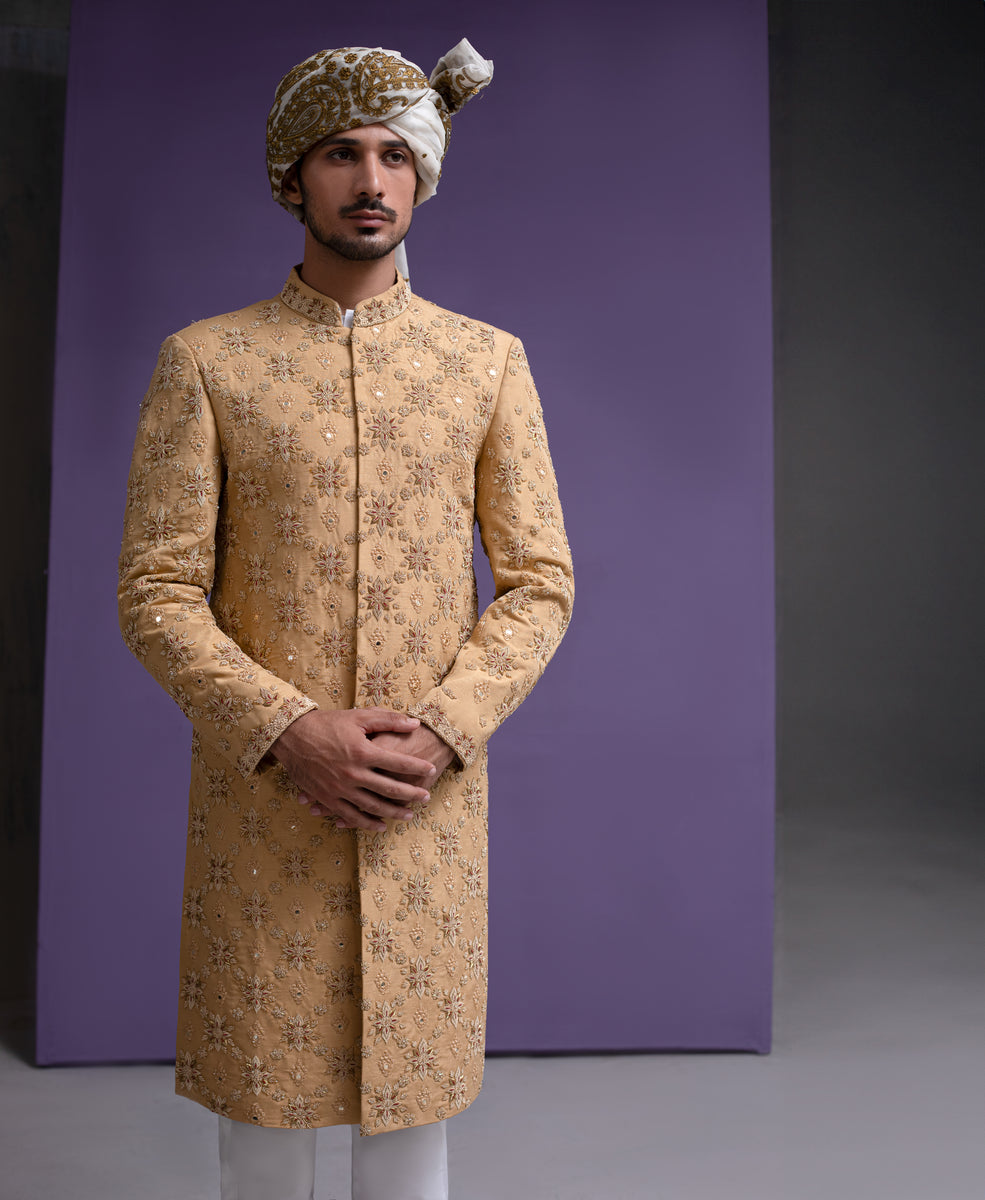 Arsalan Iqbal mustard gold luxury sherwani for men, featuring all-over floral hand-embroidery and mirror-work highlights, paired with a white and gold patterned turban.