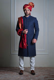 Male model wearing a navy blue sherwani with red turban by Arsalan Iqbal, luxury South Asian wedding groom attire