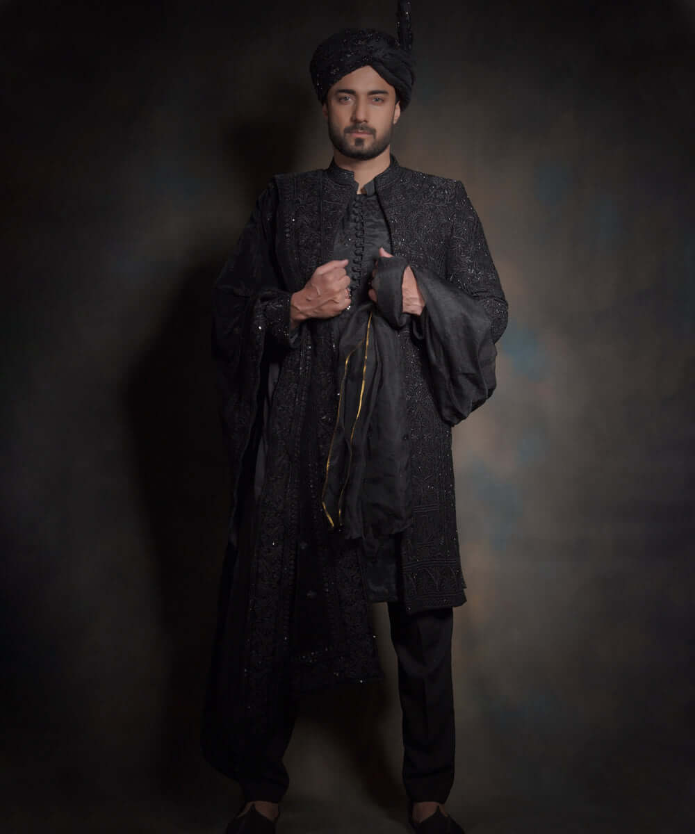 Arsalan Iqbal premium midnight black sherwani for men with tonal hand-embroidery, styled with a matching black turban, a draped silk shawl, and black traditional trousers.