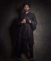 Arsalan Iqbal premium midnight black sherwani for men with tonal hand-embroidery, styled with a matching black turban, a draped silk shawl, and black traditional trousers.