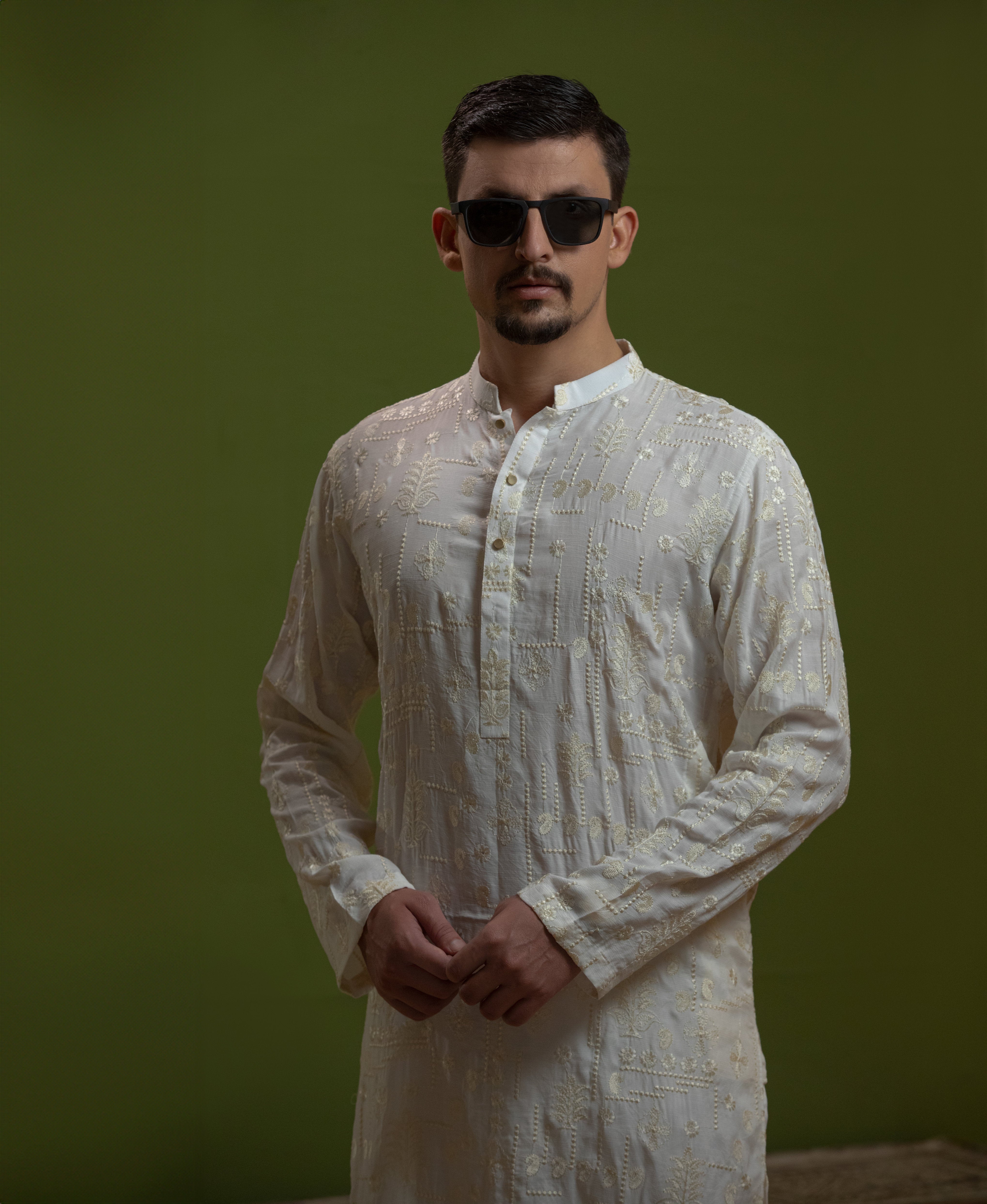 Man wearing Arsalan Iqbal's Off-White Ivory Kurta with allover silver and gold sequin embroidery, styled with black sunglasses against a deep green background
