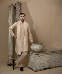 Man wearing Arsalan Iqbal's Peach & Gold Chikankari Kurta Pyjama with a cream stole draped over shoulders, styled with dark formal shoes against a warm beige backdrop