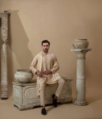 Man wearing Arsalan Iqbal's Peach & Gold Chikankari Kurta Pyjama with a cream stole draped over shoulders, styled with dark formal shoes against a warm beige backdrop