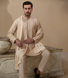 Man wearing Arsalan Iqbal's Peach & Gold Chikankari Kurta Pyjama with a cream stole draped over shoulders, styled with dark formal shoes against a warm beige backdrop
