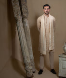Man wearing Arsalan Iqbal's Peach & Gold Chikankari Kurta Pyjama with a cream stole draped over shoulders, styled with dark formal shoes against a warm beige backdrop