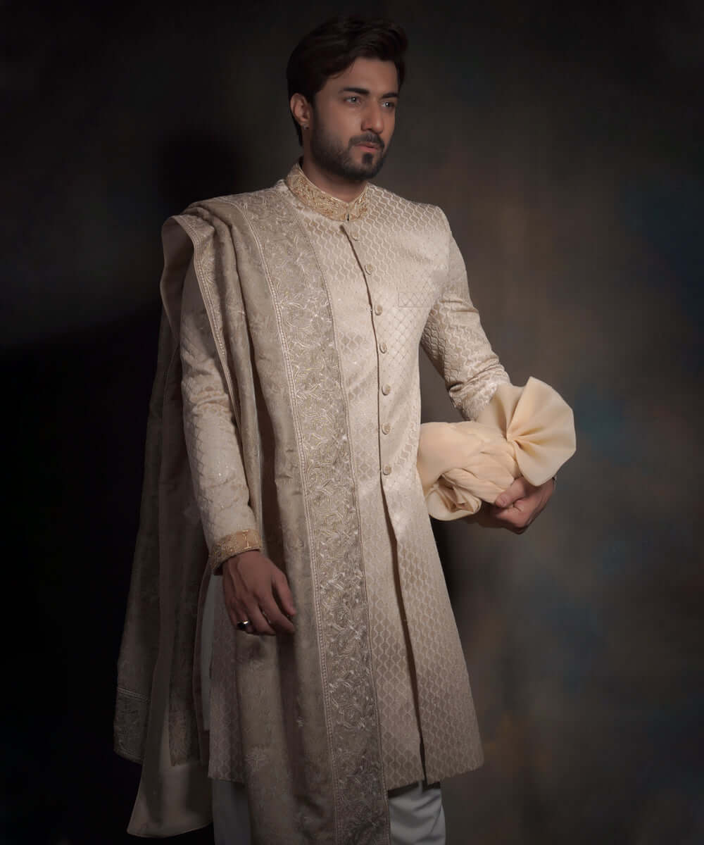 Arsalan Iqbal luxury pearl cream sherwani for men featuring a diamond-quilted pattern, an embroidered mandarin collar, and a matching draped shawl with intricate border work, held with a cream turban.