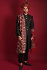 Full-length portrait of Arsalan Iqbal luxury black sherwani featuring gold buttons, paired with a matching maroon silk turban and an intricately embroidered maroon silk shawl with gold motifs, styled with black trousers and loafers.
