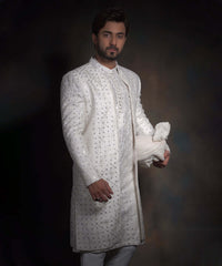 Portrait of Arsalan Iqbal snow white luxury sherwani for men, featuring geometric mirror-work, tonal embroidery, and a matching white turban with a row of decorative fabric buttons.