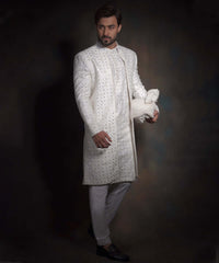 Full-length side view of Arsalan Iqbal snow white luxury sherwani featuring geometric mirror-work, styled with white formal trousers, a matching turban, and black loafers.