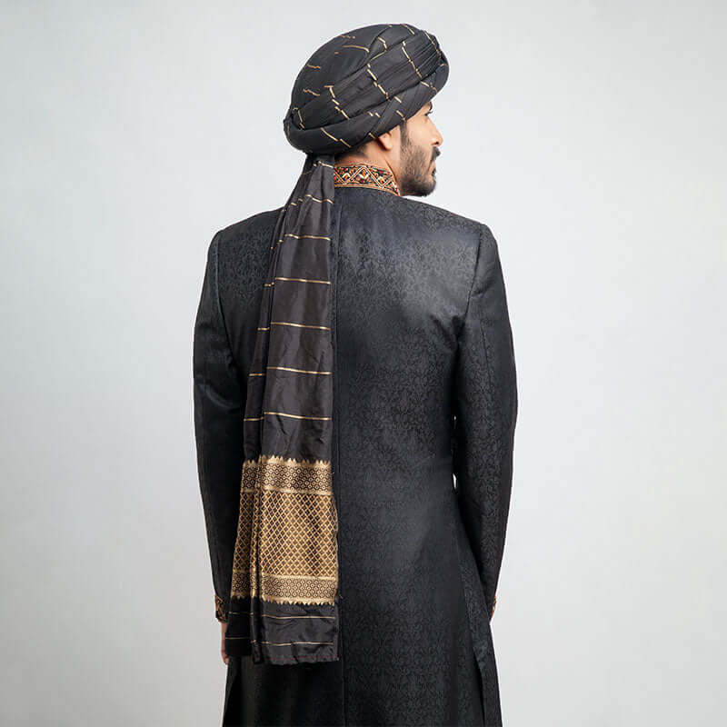 Rear view of an Arsalan Iqbal black jacquard sherwani showing the tailored fit and the long, draped tail of a gold-striped black silk turban.