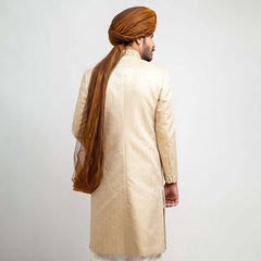 Full-length studio shot of a man in an Arsalan Iqbal black textured sherwani with a red pocket square, maroon turban, and white trousers.