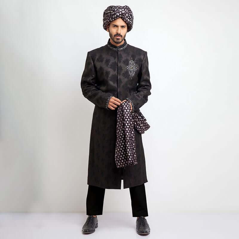 Rear view of an Arsalan Iqbal black velvet sherwani showcasing the tailored silhouette and the long tail of a gold and red dual-tone silk turban.