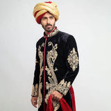 Three-quarter portrait of a man wearing an Arsalan Iqbal black velvet sherwani with intricate gold paisley chest embroidery and a gold and red dual-tone turban.