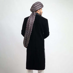 Full-length studio view of a man in an Arsalan Iqbal black velvet sherwani, paired with a silver polka dot turban and matching shawl.