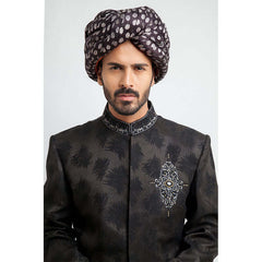 Close-up headshot of an Arsalan Iqbal charcoal grey jacquard sherwani highlighting the intricate silver and black embroidered chest emblem and a silk polka dot turban.
