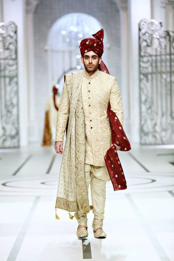 Full-length studio shot of a man in an Arsalan Iqbal black textured sherwani with a maroon pocket square, matching turban, and white trousers.