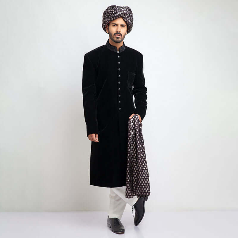 Full-length view of an Arsalan Iqbal black velvet sherwani paired with a silver polka dot turban, matching shawl, and white trousers.