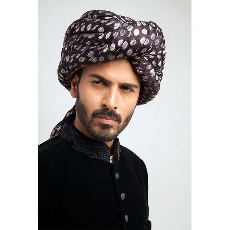 Side-profile view of a man in an Arsalan Iqbal luxury black velvet sherwani with a silver polka dot turban and matching draped shawl.
