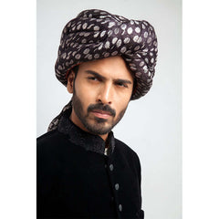 Side-profile view of a man in an Arsalan Iqbal luxury black velvet sherwani with a silver polka dot turban and matching draped shawl.