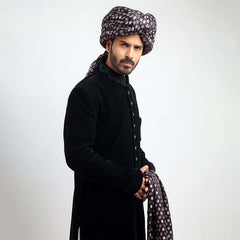 Full-length studio view of a man in an Arsalan Iqbal black velvet sherwani, paired with a silver polka dot turban and matching shawl.