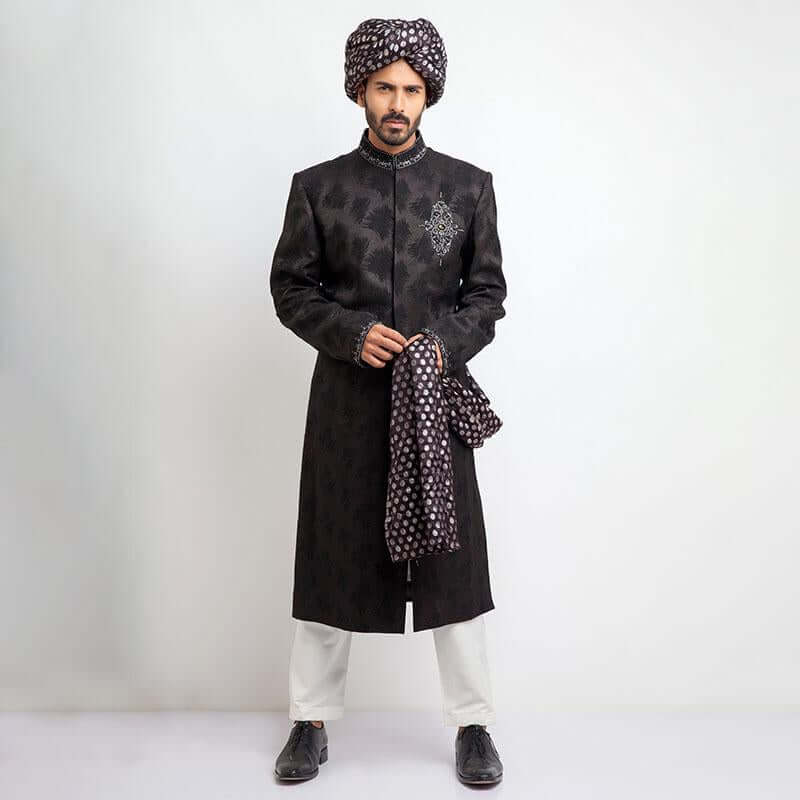 Side profile portrait of a man in an Arsalan Iqbal charcoal grey jacquard sherwani featuring silver chest embroidery and a draped silver polka dot silk shawl.