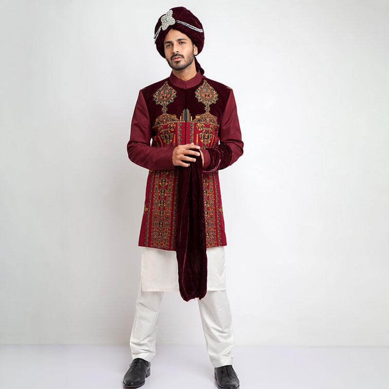 Portrait of a man in an Arsalan Iqbal cream jamawar sherwani with gold embroidered collar and cuffs, paired with a vibrant red and gold polka dot silk turban and matching shawl.