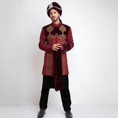 Full-length studio shot of an Arsalan Iqbal deep maroon velvet form-fitted sherwani featuring asymmetrical metallic buttons and a coordinated maroon turban.