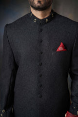 Full-length view of an Arsalan Iqbal black textured sherwani set featuring a maroon pocket square, matching turban, and white trousers.